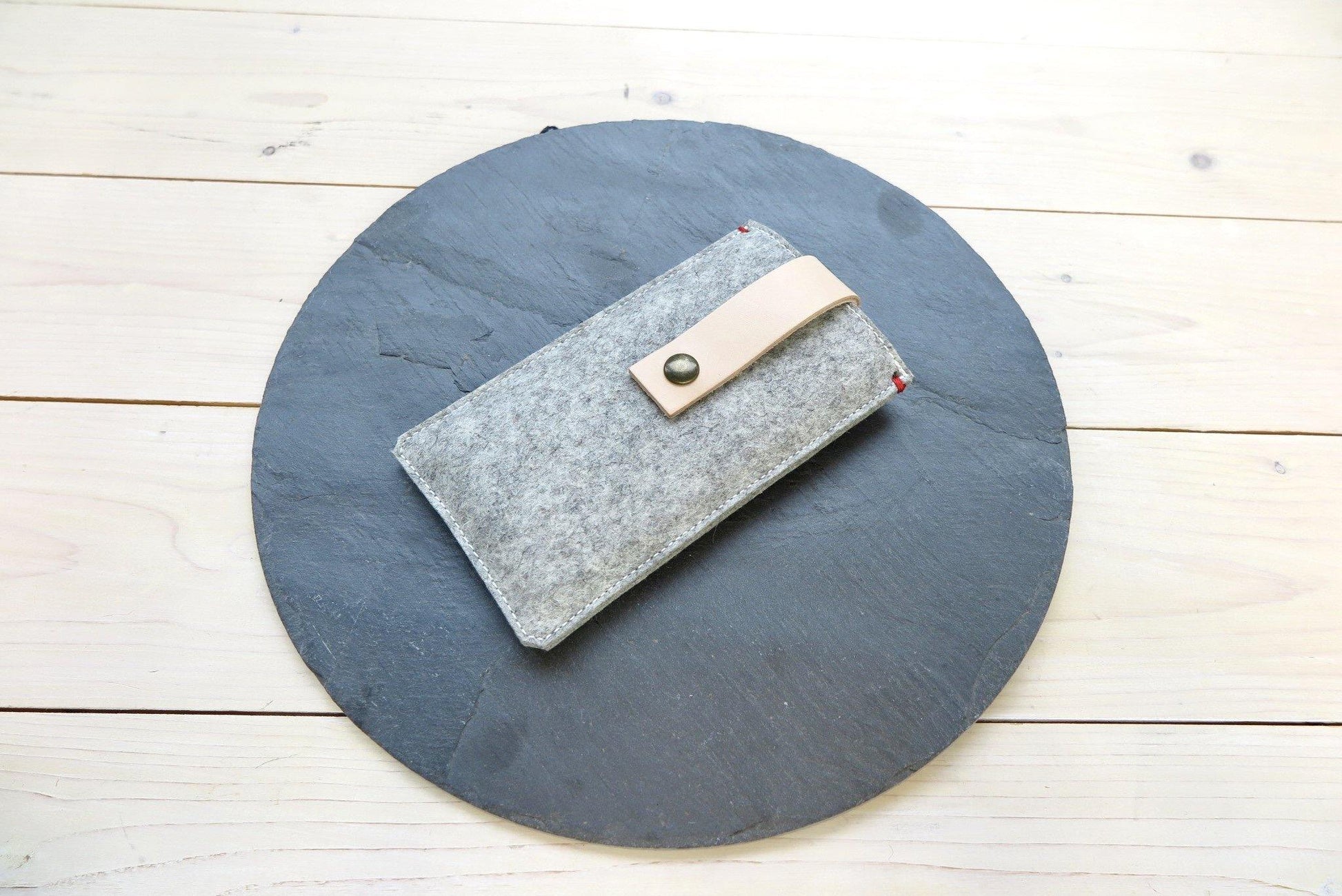 iPhone hoesje van grijs vilt met een lichte leren sluiting op een ronde leisteen. 